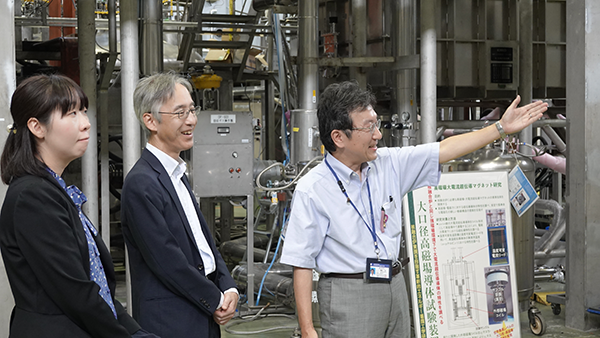 超伝導マグネット研究棟で説明を受ける恒藤審議官(中央)
